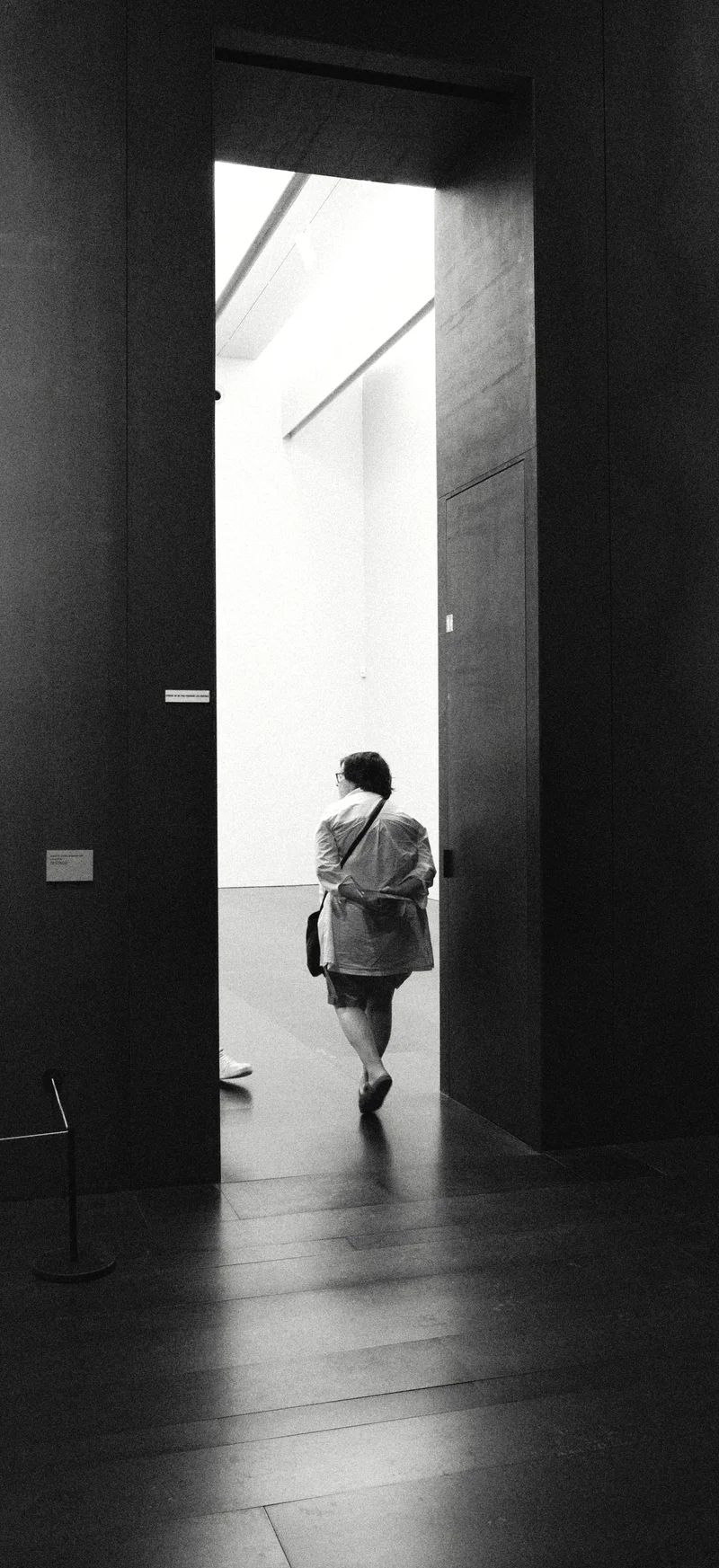 A visitor walking through a gallery doorway, seen between two dark returns.